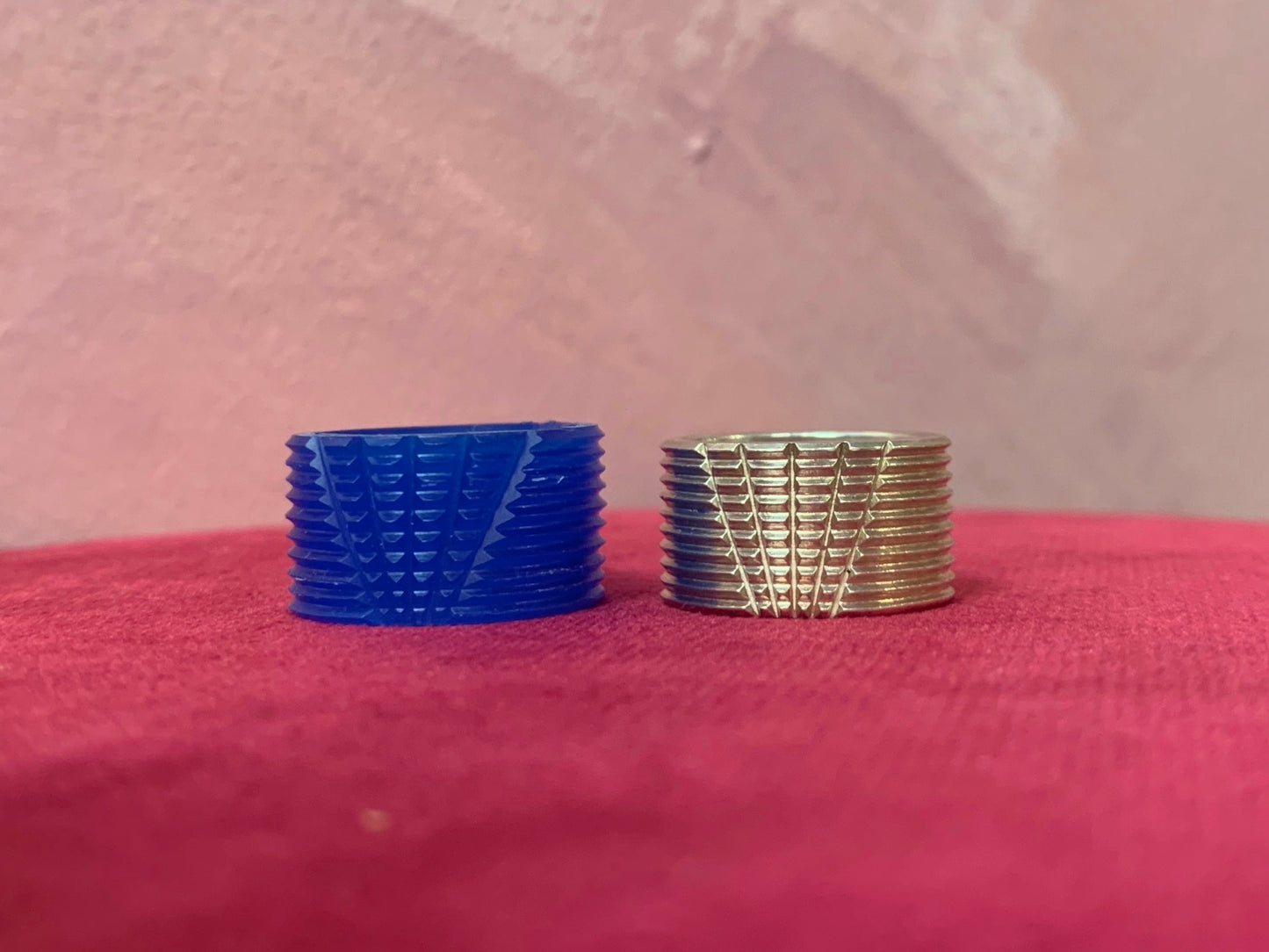 Two rings, one blue wax and one silver, on a pink surface with a textured pink background.