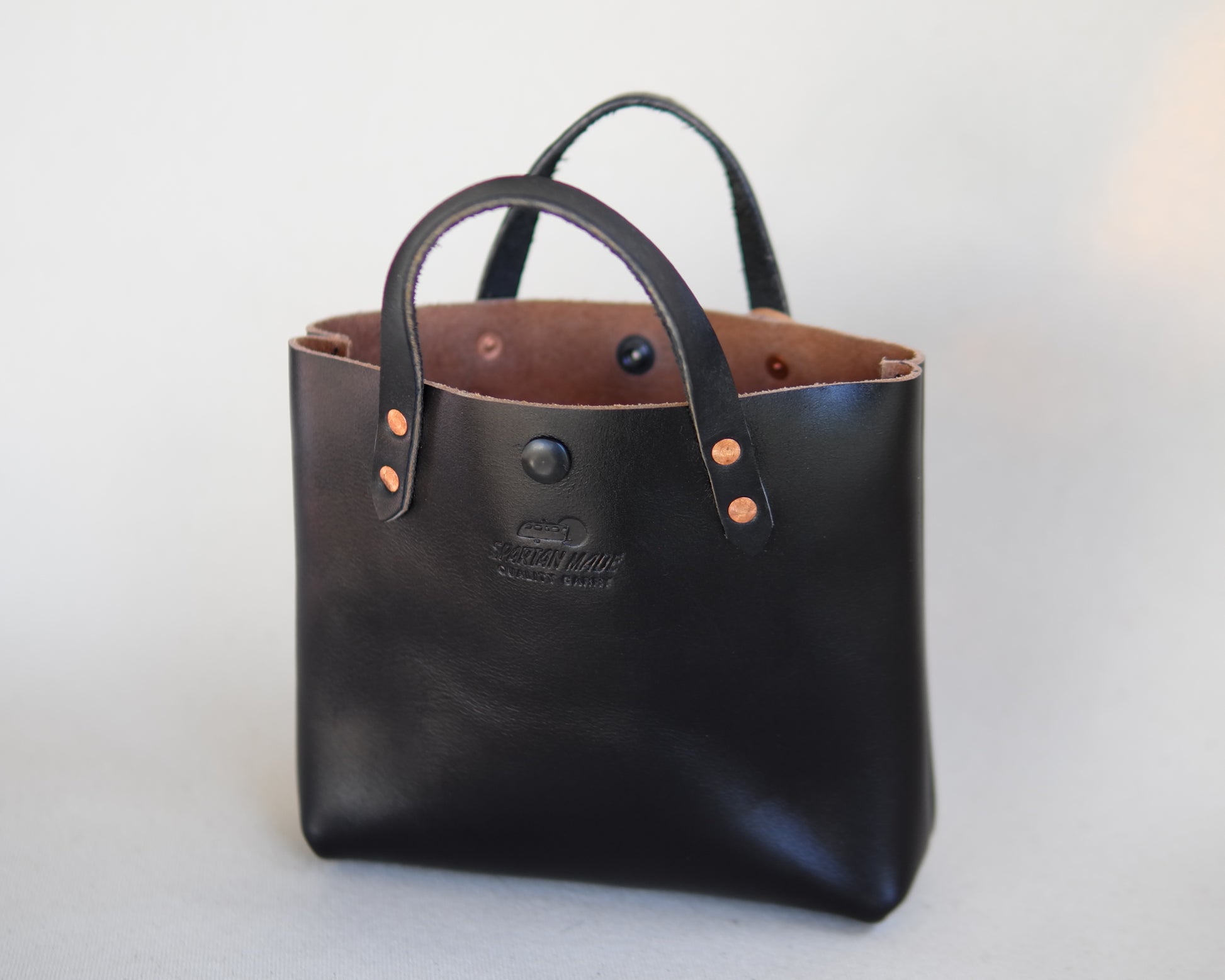 Black leather mini tote bag by Spartan Made, front view showing sleek design and structured shape.