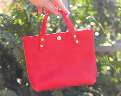 Red leather Spartan Made mini tote bag with front view, styled with hand, showcasing compact design and quality craftsmanship.