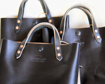 Black leather mini tote bag by Spartan Made, showcasing its compact size and sleek design.