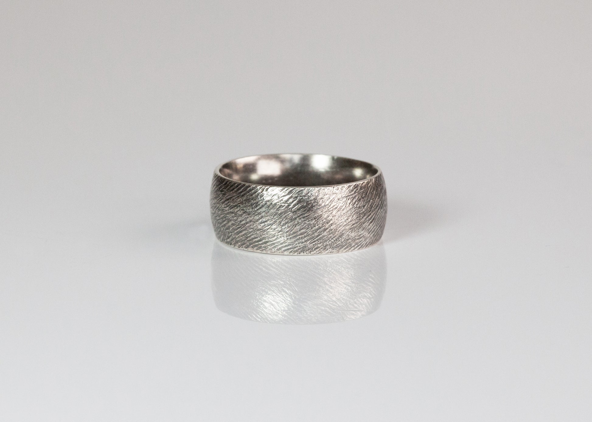 Close-up of a 10mm textured band ring by The Tiny Jeweler, showcasing its detailed, matte finish on smooth metal.