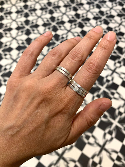 Stacking rings by Alloy Atelier featuring multiple silver bands with textured and smooth finishes, stacked together on a white background.