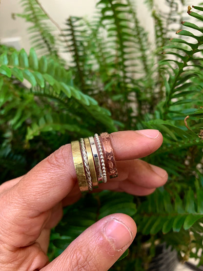 Hands holding assorted Alloy Atelier stacking rings, showcasing different styles and finishes in a close-up image.